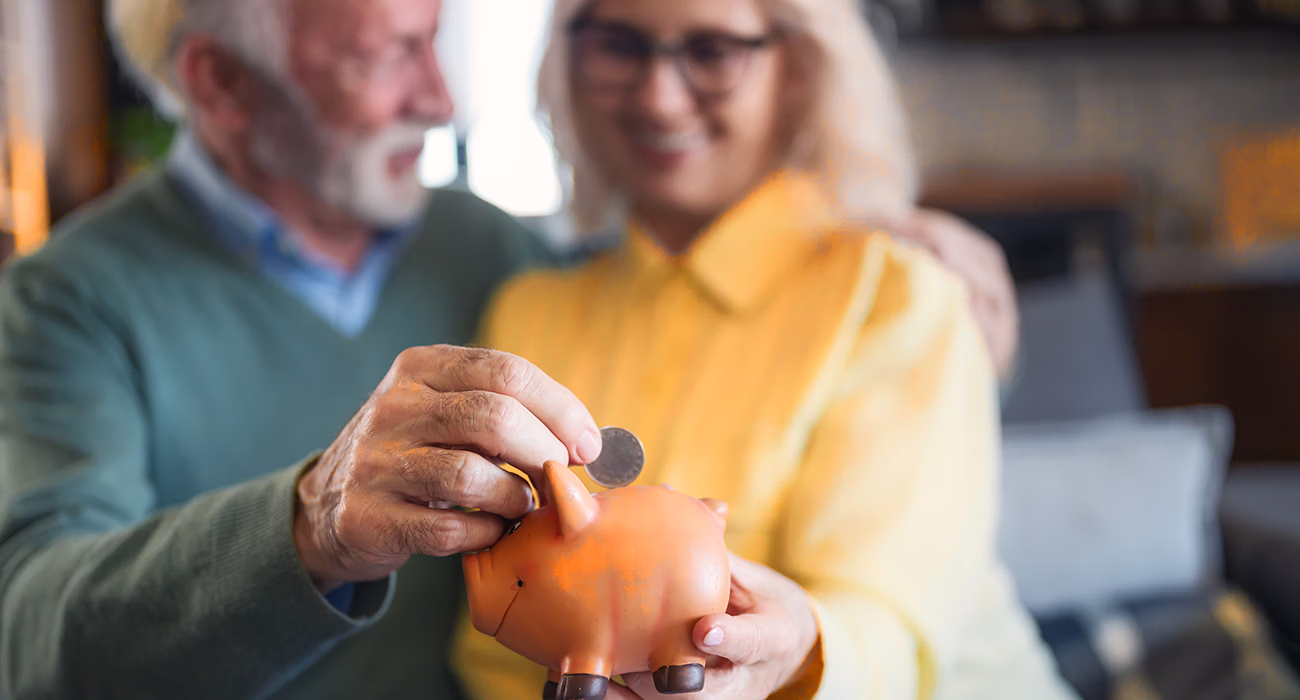 Senior couple at home putting a coin into a piggy bank